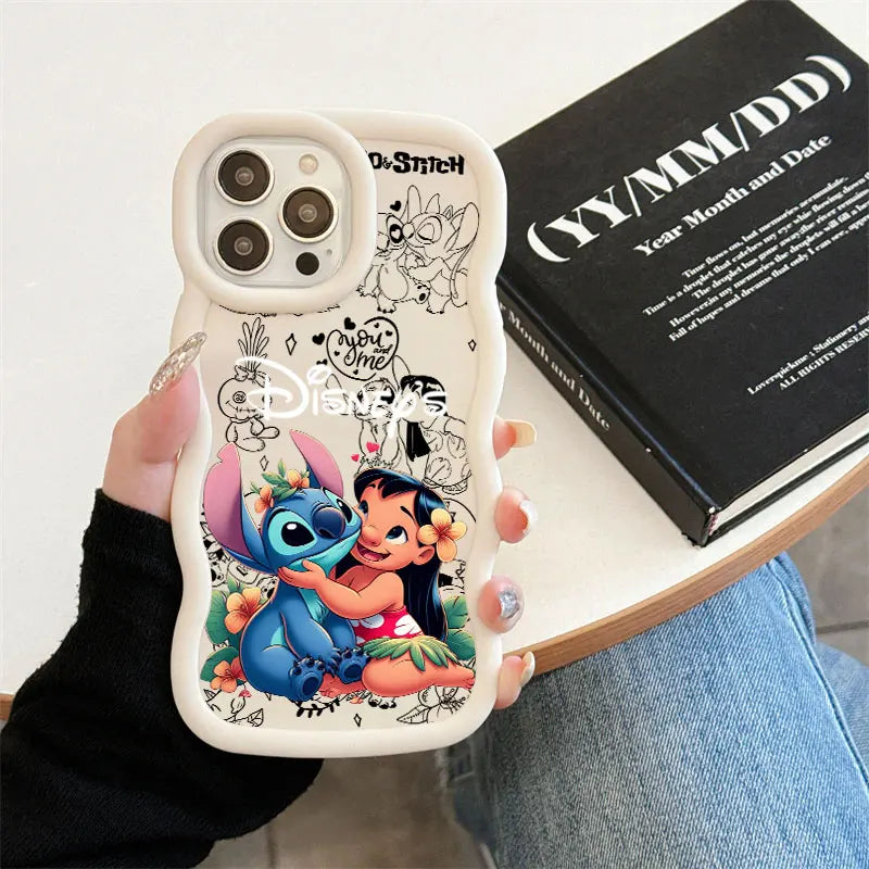 A hand holds a white phone case featuring a colorful Disney Lilo & Stitch illustration of Stitch and Lilo, with black line art characters around the border. The photo is taken in a casual indoor setting with a black book and blue jeans visible in the background.